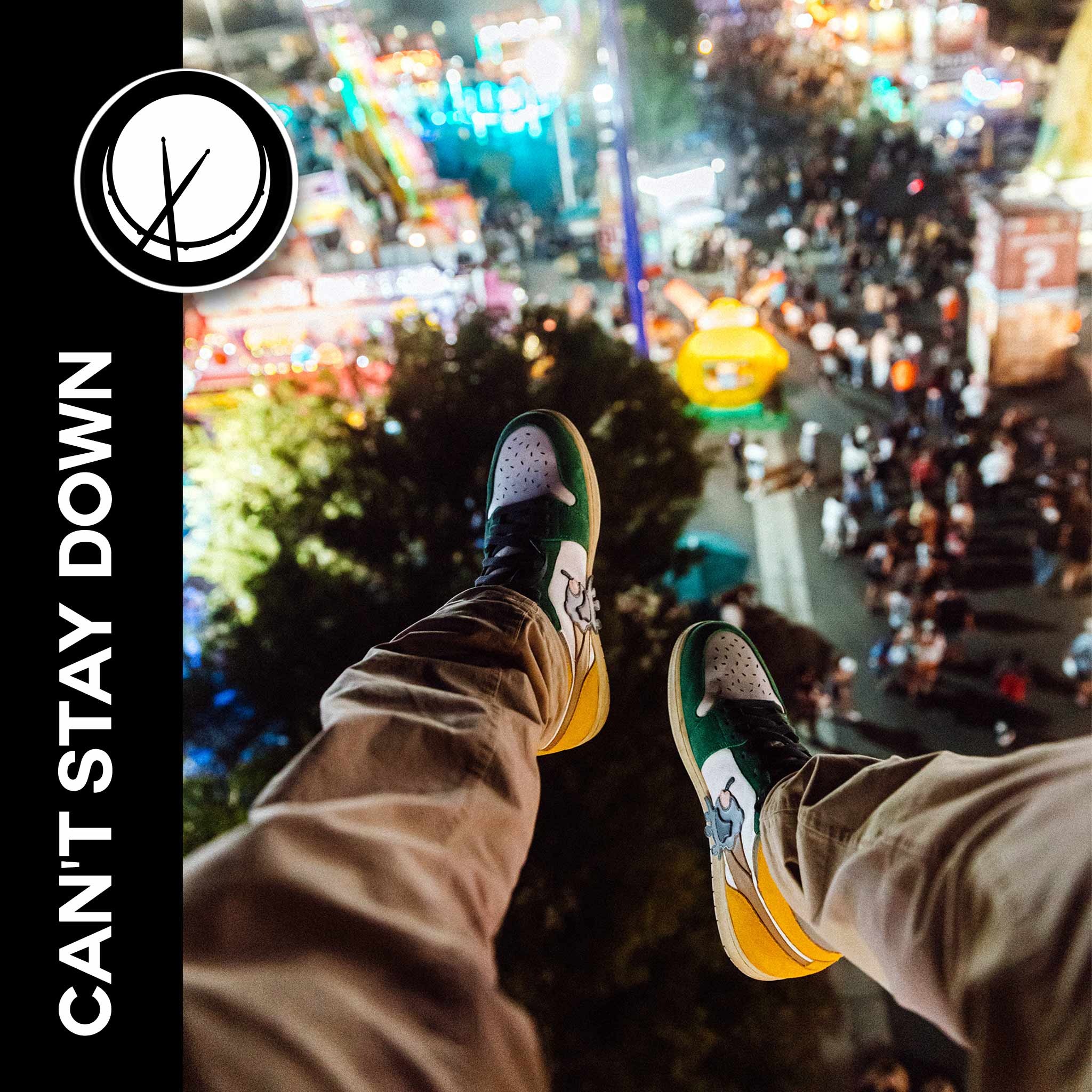 View from a really high perspective, featuring a man's sneakers looking down at a carnival. Title: "Can't Stay Down."